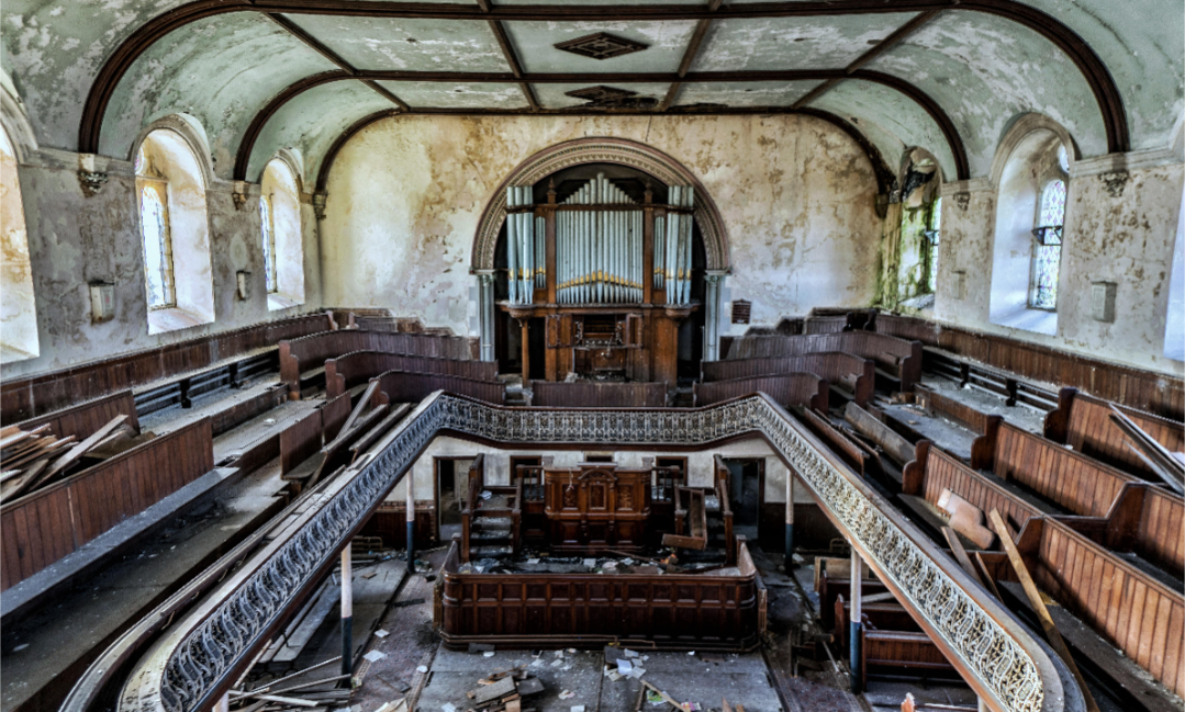 Interior of a disused Welsh chapel with wooden pews, gallery and organ