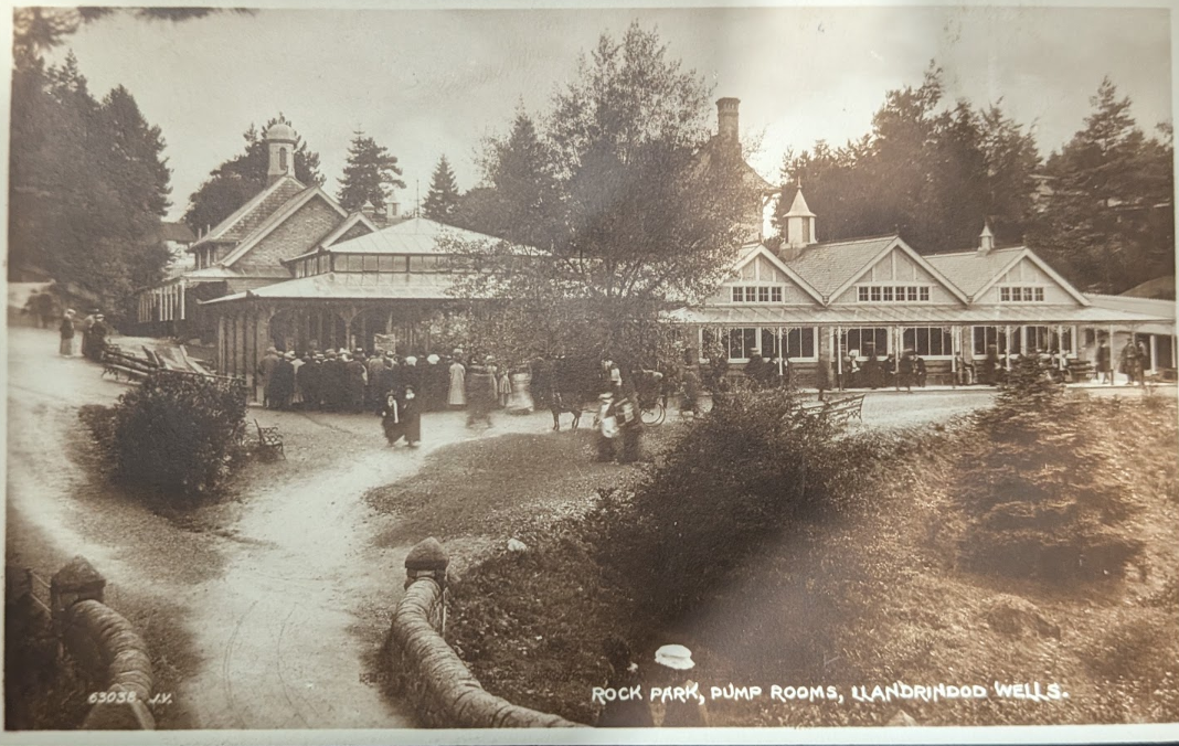 Historic postcard showing crowds of visitors outside the Rock Park Pump Rooms in Llandrindod Wells.