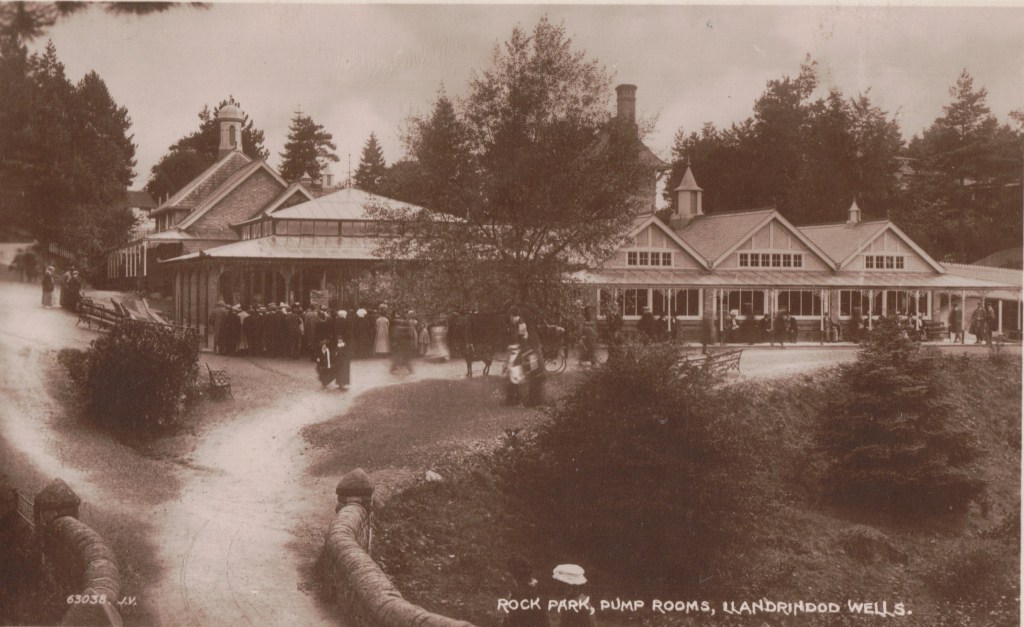 Historic postcard showing crowds of visitors outside the Rock Park Pump Rooms in Llandrindod Wells.