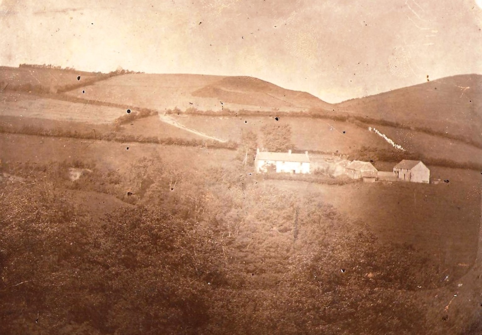 Historic sepia photograph of Caeadda near Llanwrin, showing the whitewashed farmhouse, two outbuildings and surrounding Montgomeryshire hills.