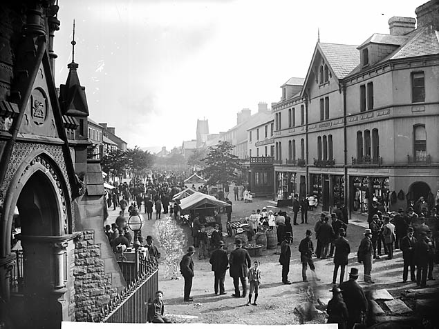 Historic photograph of Machynlleth fair around 1885, viewed from the clock tower, showing market stalls and people filling the town street.